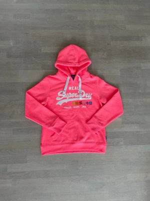 Superdry rosa hoodie  - Den är i väldigt bra skick. Men nån sten har åkt av men man ser det inte. Den är lite mindre i storleken. Storlek L men mer som M.