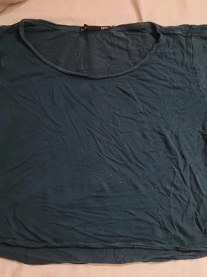 Mörkgrön croppad t-shirt - En enkel mörkgrön croppad t-shirt med rund halsringning. T-shirten är kortärmad och har en avslappnad passform, perfekt till jeans eller shorts. Materialet känns mjukt och bekvämt mot huden.