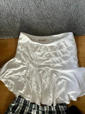 Vit kortkjol med volang - Snygg vit kortkjol med bred resår i midjan och volangig nederdel. Kjolen är i trikåtyg och är perfekt för dig som gillar en feminin och fräsch stil. Passar till många olika outfits och är enkel att matcha.