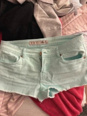 Mintgröna denimshorts från Denim Co - Snygga mintgröna shorts från Denim Co i klassisk denimstil med fem fickor, råa kanter och knapp- samt dragkedjestängning. Perfekta för varma dagar och ger en fräsch look till din outfit.
