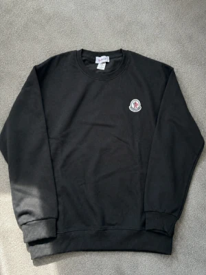Svart sweatshirt från Moncler - Svart sweatshirt från Moncler med rund halsringning och ribbade muddar. Liten Moncler-logga på bröstet och stor vit Moncler-M med logga på ena ärmen. Perfekt för en clean och stilren look, Den är storlek M men jag skulle säga att den passar S mer.
