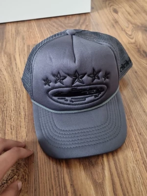 Grå meshkeps med broderade stjärnor (Corteiz) - Snygg grå keps med mesh på sidorna och broderade svarta stjärnor framtill. Kepsen har böjd skärm och justerbar baksida. Perfekt för en avslappnad streetwear-look.
