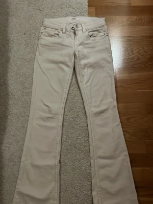 Beige/vit lowwaist bootcut jeans   - Säljer ett par beige/vita snygga beige bootcut jeans med broderade detaljer på bakfickorna. Lågmidjade i passform. Endast använt 1 gång.