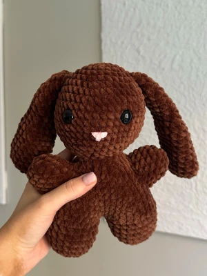 Brun virkad kanin - Virkat gosedjur i velvetgarn. Kaninen är 26cm lång och tillverkad för hand, vilket gör varje kanin unik. Kaninen har svarta säkerhetsögon som sitter fast från insidan. Rekommenderas dock inte för de allra minsta barnen, då det alltid finns en viss risk, vid hårt drag, att de lossnar. Perfekt som present eller mysig inredningsdetalj! Tvättråd: max 30°C, handtvätt.