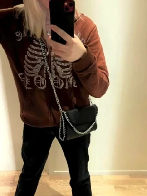 Brun hoodie - Säljer en brun hoodie med dragkedja och huva. Hoodien har fickor framtill och en avslappnad passform, perfekt för en cool streetstyle-look.
