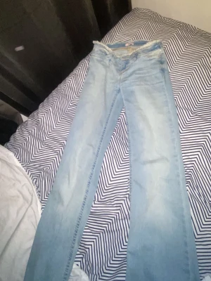 Nelly Ljusblå lågmidjade bootcut jeans - Säljer ett par ljusblå nelly bootcut jeans med låg midja och klassisk femficksdesign i storlek 32/xxs. Jeansen har en avslappnad passform och är tillverkade i denim med lätt tvättad look. Perfekta för en trendig och avslappnad stil.