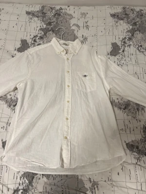 Vit linneskjorta med knappstängning från Gant - Klassisk vit skjorta från Gant i linne med lång ärm och knappstängning framtill. Skjortan har en bröstficka med broderad logga och en avslappnad passform. Perfekt för en stilren och fräsch look.