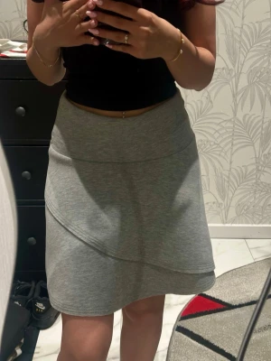 Grå omlottkjol i bomull - Snygg grå kjol med omlott-look och mjukt bomullsmaterial. Kjolen har en kort längd och en enkel, stilren design som passar perfekt till vardagsoutfits. Ordinarie pris: 299kr