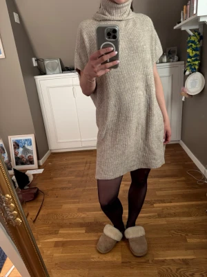 Beige stickad poloklänning - Mysig beige stickad klänning med polokrage och lös passform. Klänningen är kort och har ett ribbat mönster, perfekt för lager-på-lager-stil. Ärmlös design som ger en avslappnad och trendig look.