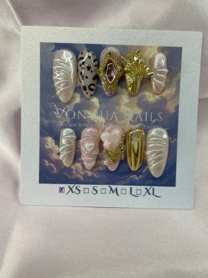 AngelRelic (XS);Medium Almond - Handgjorda press-on naglar i en medium lång mandelform med pärlvit bas, marmorerade detaljer, guldiga 3D-dekorationer och en nagel med brun leopardmönster. Mix av glansiga och metallic ytor, vissa med swirl-design och hjärtformad dekoration. Perfekt för dig som vill sticka ut.XS: 14 mm, 11 mm, 11,5 mm, 10 mm, 8 mm 