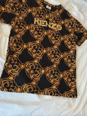Svart t-shirt med tigertryck från Kenzo - Cool svart t-shirt från Kenzo med gult tigertryck över hela plagget och Kenzo-logga på bröstet. T-shirten har rund hals och korta ärmar. Perfekt för dig som vill sticka ut med ett unikt mönster och streetwear-vibe.