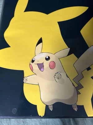 Pokémon pärm med Pikachu-motiv - Säljer en svart pärm med stort gult Pikachu-tryck på framsidan. Perfekt för att samla Pokémonkort eller andra samlarkort. Pärmen har en tydlig och färgglad design med Pikachu i fokus.