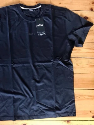 Svart t-shirt från BOSS - Svart t-shirt från BOSS med diskret logga på bröstet. Klassisk rund halsringning och korta ärmar. Tillverkad i mjuk bomull som känns skön mot huden. Perfekt för en clean och stilren look.