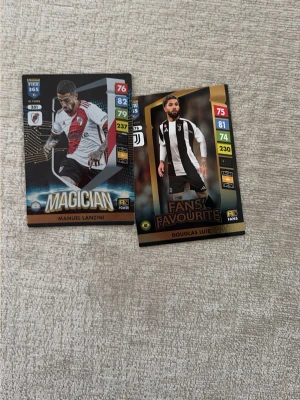 FIFA 365 samlarkort fotboll - Två FIFA 365 samlarkort med fotbollsspelare, en med svart, vit och röd design och en med svart och vit design. Kortens motiv är spelare i matchställ och har text som 'MAGICIAN' och 'FANS' FAVOURITE'. Perfekt för dig som gillar att samla på sportkort.