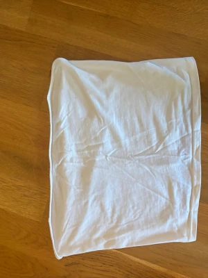 Tubtopp - Enkel och stilren vit bandeau tubtopp i mjuk bomull. Perfekt att matcha med jeans eller kjol för en clean look. Ärmlös och axelbandslös design som sitter tight mot kroppen.