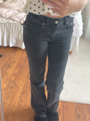 Svarta bootcut jeans med fickdetaljer - Snygga svarta bootcut jeans med coola ficklock och silvriga knappar bak. Jeansen har hög midja och klassisk femficksdesign. Perfekta för dig som gillar en avslappnad men trendig stil. 
