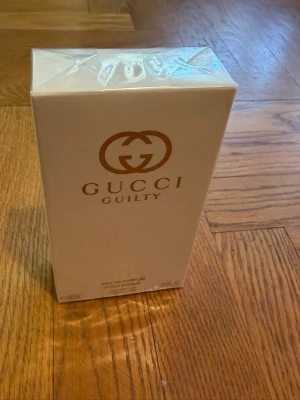 Gucci Guilty Eau de Parfum 90ml - Gucci Guilty Eau de Parfum i en elegant, ljusbeige kartong med guldiga detaljer och logotyp. Förpackningen är rektangulär och tillverkad av kartong. Parfymen är på 90 ml och passar dig som gillar lyxiga dofter från ett välkänt märke.