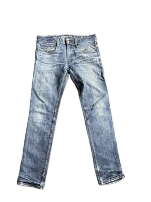 Blå Replay jeans - Säljer ett par blå jeans från Replay med snygga slitningar och klassisk femficksdesign. Jeansen har raka ben och detaljer som Replay-logga på fickan. Perfekta för en avslappnad och trendig stil.