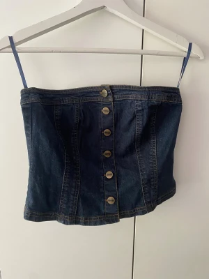 Mörkblå denim tubtopp med knappar - Snygg mörkblå tubtopp i denim med smala axelband och dekorativa knappar framtill. Knappt använd 