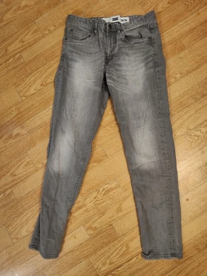 Grå jeans herr stl 34/34 - Snygga grå jeans med klassisk femficksdesign och diskreta slitningar framtill. Jeansen har normal midja och raka ben, perfekta för en avslappnad och trendig look. Herr stl 34/34. Jag tror att det finns någon liten på dessa men hittar inte var den sitter nu. 