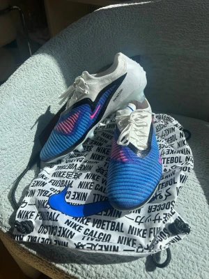 Nike Phantom 6 Elite Low Cut FG Attack Fotbollsskor Blå/Rosa/Vit EU 45.5 - I princip helt nya fotbollsskor. Använda max 60 minuter på konstgräs men tyvärr lite för små för mig.  Nypris: 3099 på Unisportstore Köpta för 2319 med rabatt Säljs för 1599 vid snabb och smidig affär