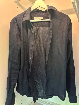 Mörk blå linneskjorta från Dressmann - Snygg svart skjorta från Dressmann i premium linne. Skjortan har klassisk krage, knäppning framtill och långa ärmar. Perfekt för dig som gillar en stilren och luftig look. Storlek s 