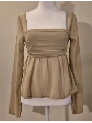 Beige topp i storlek XS. Nypris 399 kr - Långärmad blus med fyrkantig halsringning och smockdetaljer baktill. Blus BT Maddie i storlek XS. Färgen heter Wheat. Tunn och genomskinlig. Material 100 % polyester. Midjebredd ca 32 cm och längd ca 54 cm. 710/50
