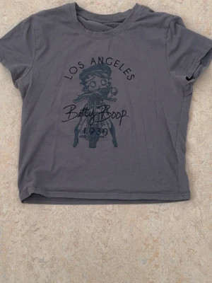 Grå Betty Boop t-shirt Los Angeles - Cool grå t-shirt med Betty Boop-tryck och texten 'Los Angeles' framtill. T-shirten har rund halsringning och korta ärmar.