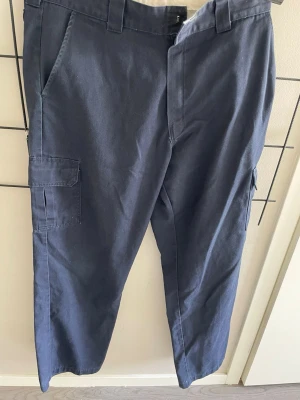 Mörkblå oversized cargobyxor från Dickies - Snygga mörkblå cargobyxor från Dickies med raka ben och flera praktiska fickor på sidorna. Byxorna har bälteshällor och är tillverkade i ett slitstarkt bomullsmaterial. Perfekta för en avslappnad streetstil.