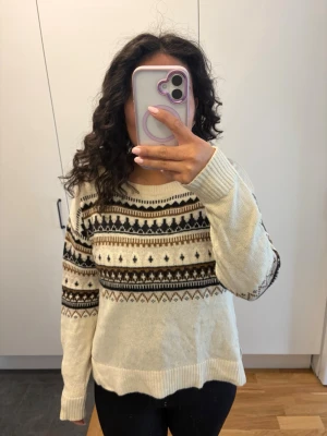 Beige stickad tröja med mönster - Mysig beige stickad tröja med klassiskt nordiskt mönster i svart och brunt. Tröjan har rund halsringning, långa ärmar och ribbade muddar. Perfekt för kalla dagar och ger en chill vibe till din outfit. Vet tyvärr inte storleken men skulle säga att den passar S/M beroende på hur man vill att passformen ska vara☺️