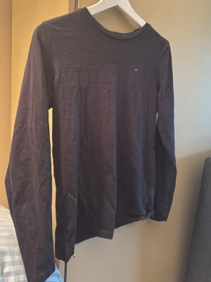 Svart långärmad topp Tommy Hilfiger - En stilren svart långärmad topp från Tommy Hilfiger i mjuk ekologisk bomull. Klassisk rund halsringning och diskret logga på bröstet. Perfekt för en clean och enkel look.