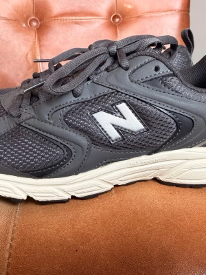 New Balance sneakers grå - Snygga grå sneakers från New Balance med vit sula och klassisk N-logga på sidan. Ovandelen är i mesh och syntetmaterial för bra andningsförmåga och komfort. Perfekta för en sportig och avslappnad stil.