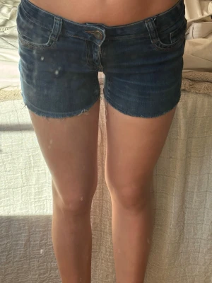 Mörkblå jeansshorts med rå kant - Snygga mörkblå jeansshorts med rå, fransig kant och klassisk femficksdesign. Shortsen har låg midja och stängs med knapp och dragkedja. 