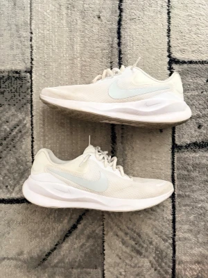  Nike revolution sneakers  - Säljer ett par vita Nike sneakers med lågt skaft och klassisk swoosh i ljusgrått på sidan. Skorna har ovandel i mesh för bra ventilation och en bekväm, vadderad sula. Perfekta för dig som gillar stilrena och sportiga sneakers.