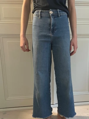 Blåa raka jeans med rå kant - Snygga blå jeans med hög midja, bootcut och raka ben. Jeansen har råa, fransiga benslut och klassiska fem fickor. Perfekta för en avslappnad och trendig look. Tillverkade i denim med en ljusblå tvätt.