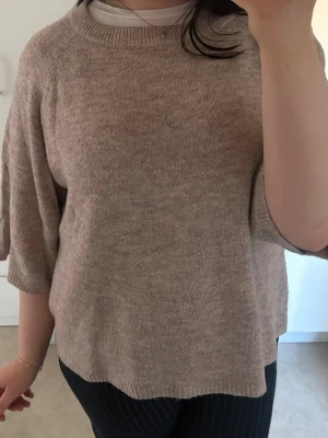 Beige stickad tröja med halvlånga ärmar - Mjuk och enkel beige stickad tröja med halvlånga ärmar och rund halsringning. Tröjan har en avslappnad passform och är perfekt för lager på lager. Inga synliga loggor eller mönster, bara en clean och stilren look.