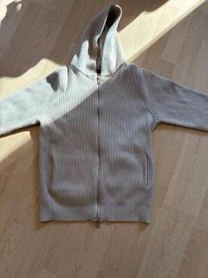 Beige ribbad hoodie från Brand Island - Snygg beige hoodie från Brand Island i ribbat material. Dragkedja hela vägen framtill, två fickor och stor huva. Perfekt för en chill och avslappnad stil. Materialet känns mjukt och skönt mot huden. Nypris=1400
