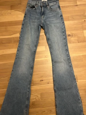 Blå bootcut jeans med hög midja - Säljer ett par ljusblå bootcut jeans med hög midja och klassiska fem fickor. Jeansen har en snygg utsvängd passform och är tillverkade i denim. Perfekta för dig som gillar retrostil och vill ha ett par jeans som sticker ut. E lite söndriga vid slutet av jeansen