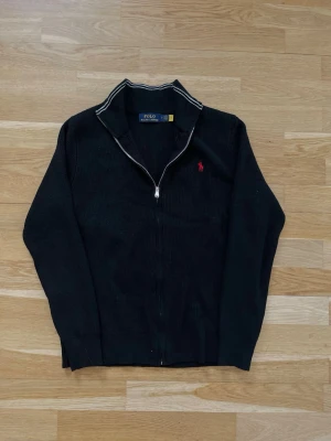 Polo Ralph Lauren kofta - En stilren och snygg tröja i mycket fint skick, endast använd några få gånger och känns nästan som ny. Den har inga fläckar, slitningar eller andra skador.  Materialet är tjockt och varmt, vilket gör den perfekt för kallare dagar under höst, vinter och vår. Den fungerar lika bra till en mer elegant outfit som till en avslappnad vardagsstil.  * Storlek: M * Passform: Normal (modell: 178 cm / 70 kg) * Skick: Väldigt bra, nära nyskick  Skriv gärna om du har frågor eller är intresserad!
