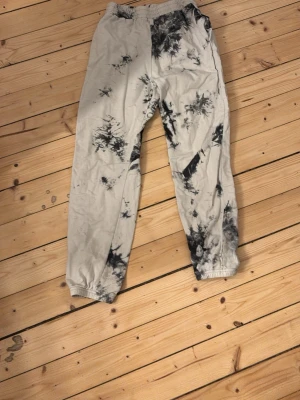Svarta och vita tie-dye mjukisbyxor - Unika mjukisbyxor med svart och vit tie-dye mönster. Byxorna har elastisk midja och muddar vid benslut för en skön passform. Perfekta för chill dagar och att hänga med kompisar. Materialet känns mjukt och bekvämt mot huden.