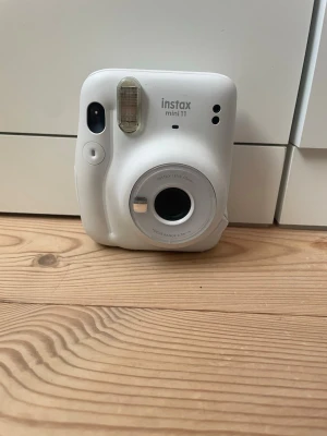 Insta mini 11  - Säljer en vit Fujifilm Instax Mini 11 direktfilmskamera. Kameran har en rundad form, inbyggd blixt och enkel knapp för att ta bilder. Tillverkad i plast med detaljer i silver runt objektivet. Perfekt för att ta instant-bilder och få foton direkt i handen.