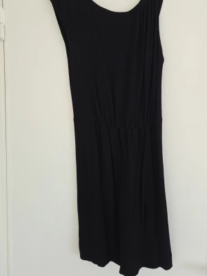 Svart ärmlös klänning - En enkel och stilren svart klänning med ärmlös design och rund halsringning. Klänningen har en lätt rynkad midja som ger en snygg passform och faller mjukt. Den har även en dragkedja i sidan för bättre passform. Perfekt för dig som gillar minimalistisk stil och vill ha något som är lätt att matcha.