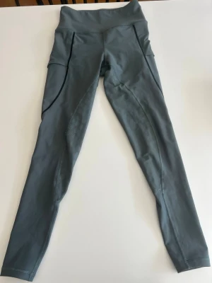 Grå sportiga ridbyxor med hög midja - Säljer ett par grå Maya delorez ridbyxor med hög midja och snygga detaljer längs benen. De har diskreta sömmar och paneler med mönstrad struktur på sidorna. Perfekta för träning eller chill. Materialet är stretchigt och bekvämt.
