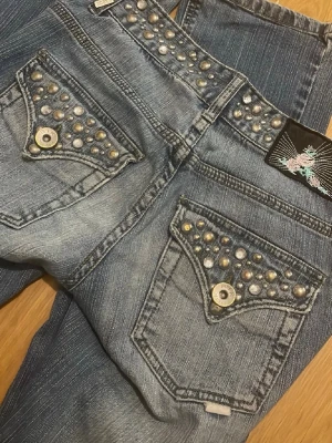 Blå jeans med nitar från Bik Bok - Säljer ett par blå jeans från Bik Bok med coola silverfärgade nitar på fickorna och linningen. Jeansen har en klassisk femficksmodell och är gjorda i denim med snygg tvättad look. Perfekta för dig som vill sticka ut lite extra! 💛