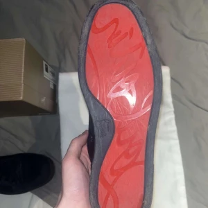 Mörk blåa Louboutin  - Säljer ett par eleganta mörk blåa sneakers från Christian Louboutin i mocka. Skorna har den ikoniska röda sulan och snörning framtill. Perfekta för den som vill ha en stilren look med en touch av lyx.