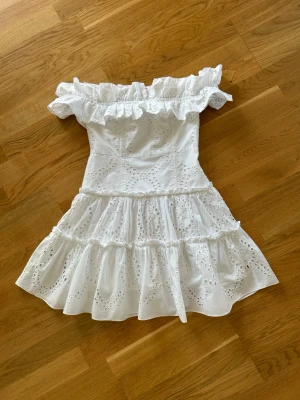  Ny slutsåld Vit offshoulder student klänning med volang från Zara  - Supersöt vit kortklänning med offshoulder och volangdetaljer. Klänningen har broderade spetsmönster och flera lager i kjolen för extra volym. Perfekt för sommarens alla tillfällen och ger en romantisk vibe.