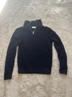 Mörkblå stickad halvzip-tröja - Mörkblå stickad tröja med halv dragkedja och hög krage. Tröjan har långa ärmar och ribbade muddar vid ärmslut och nederkant. Perfekt för lager på lager och en clean look.