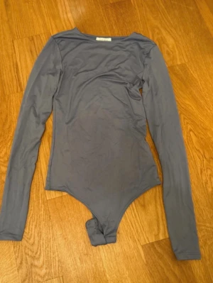 Grå långärmad body från Amisu - Säljer en stilren grå body från Amisu i storlek XXS. Bodyn har långa ärmar och rund halsringning, tillverkad i ett mjukt och stretchigt material som sitter snyggt på kroppen. Perfekt att matcha med jeans eller kjol.