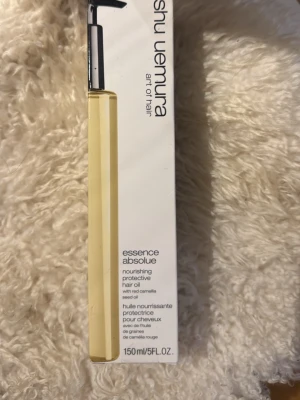 Shu Uemura Essence Absolue hårolja OANVÄND - Shu Uemura Essence Absolue nourishing protective hair oil i en genomskinlig gul flaska med svart pump. Innehåller kameliafröolja och ger näring och skydd till håret. Flaskan rymmer 150 ml och har en stilren, lyxig design. Nypris 1200 