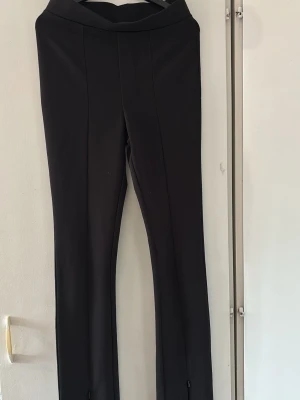 Svarta slim byxor med dragkedja - Svarta byxor med slim passform och diskreta dragkedjor vid bensluten. Snyggt skräddad midja och raka ben, perfekta för en clean och stilren look. Materialet känns mjukt och stretchigt, vilket gör dem bekväma att bära hela dagen. Passar perfekt för dig som vill vara lite stiligare i din vardag eller större event. 
